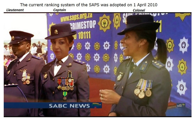 Gruppe von Menschen in Uniformen und Hüten, die mit einem Banner stehen, mit Text oben und unten, der besagt "Das aktuelle Ranglistensystem der SAP wurde am 1. April 2010 eingeführt."