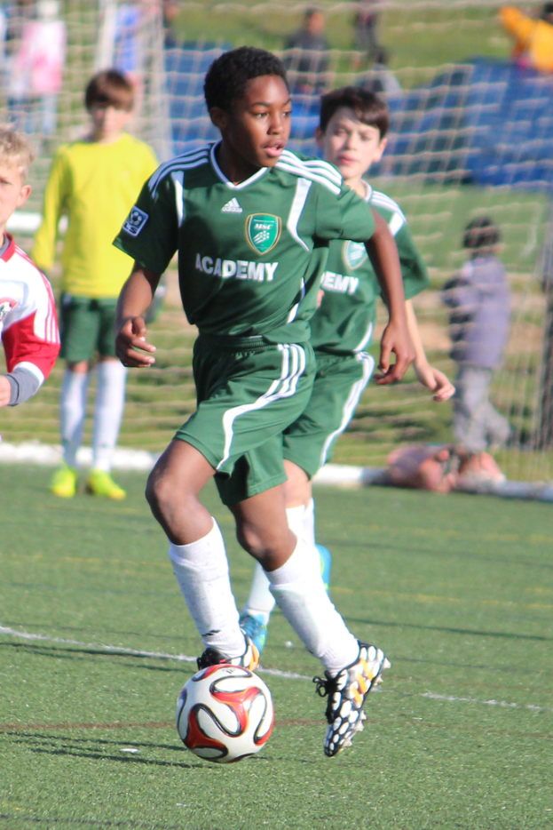 Zwei Personen spielen Fussball in einem Stadion mit wenigen Zuschauern und einem Netz im Hintergrund.
