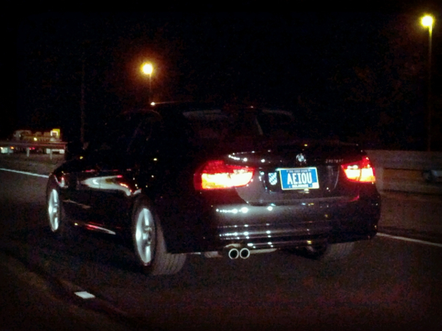 Ein schwarzer Wagen mit Leuchten und einer Aufschrift steht in der Mitte einer Straße, vor einem schwarzen Hintergrund mit Leuchten.