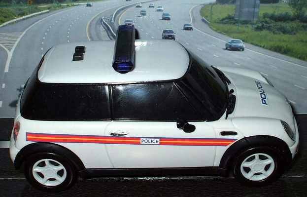 Weißes Polizeiauto mit "Polizei" darauf fahrend auf einer Straße außerhalb der Stadt, umgeben von bewegendem Verkehr, Gras und Bäumen auf beiden Seiten.