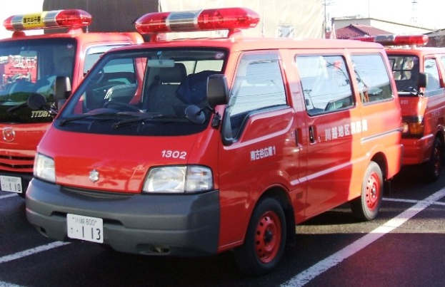 Drei rote Rettungswagen mit weißer und schwarzer Detailierung nebeneinander auf einem Parkplatz geparkt, mit Gebäuden, Polen und einem klaren blauen Himmel im Hintergrund.