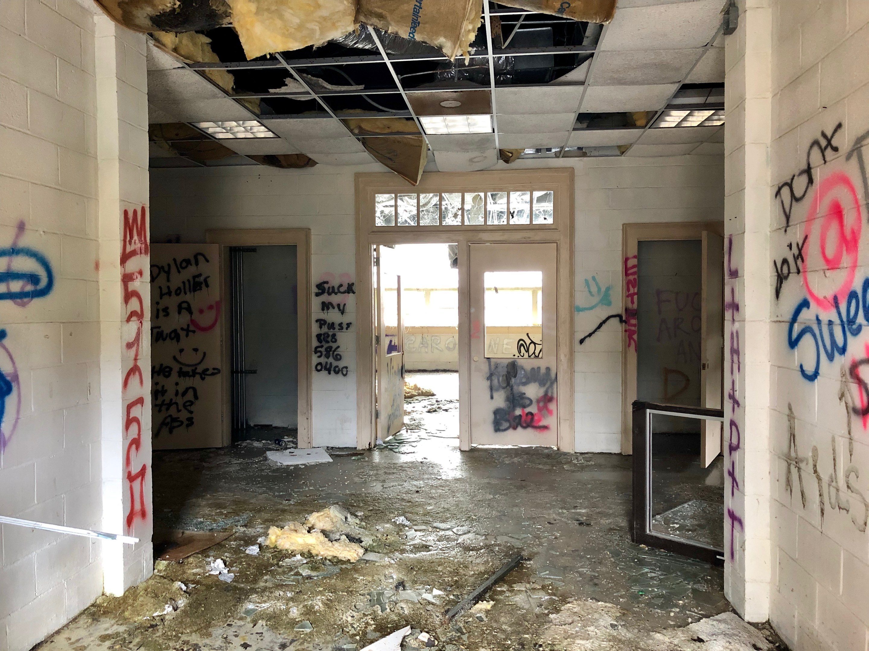 Verlassenes Gebäude mit graffiti-bedeckten Wänden und Decke, Schutt auf dem Boden, Türen und Fenster im Hintergrund und verstreute Gegenstände.