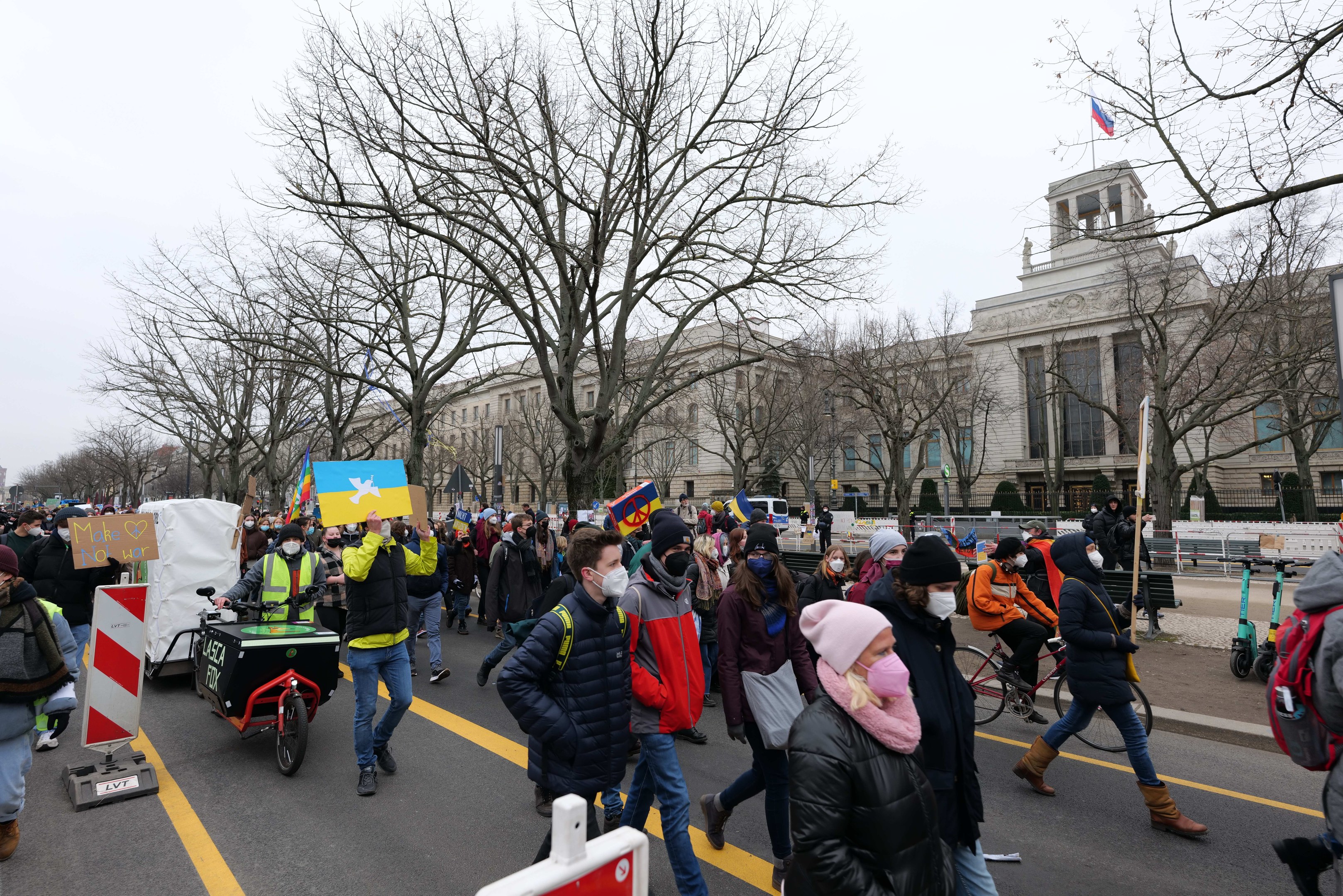 Ein großer Protestmarsch in Washington, D.C. am 21. Januar 2020, mit Menschen, die marschieren, Schilder halten und Fahrräder fahren, vor einem Gebäude auf einer Straße, unter einem klaren blauen Himmel.