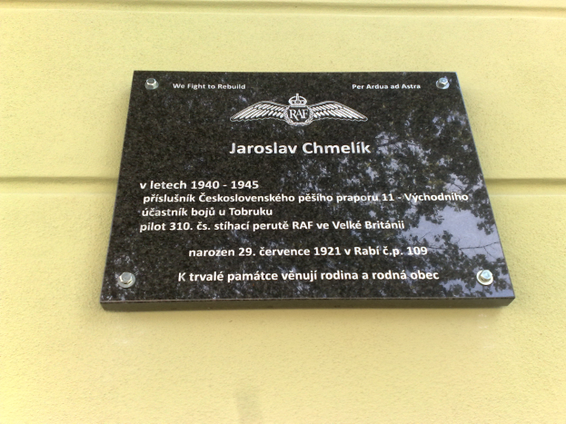 Eine schwarze Plakette mit weißer Schrift, die "Jaroslav Chmelik" lautet und von einem dekorativen Rahmen umgeben ist, die an einer Gebäudewand angebracht ist.