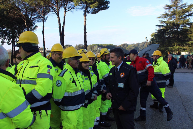 Eine Gruppe von Menschen in gelben Westen und Helmen, einige mit Mützen, die zusammen auf einer Straße stehen, umgeben von Bäumen unter einem klaren blauen Himmel.