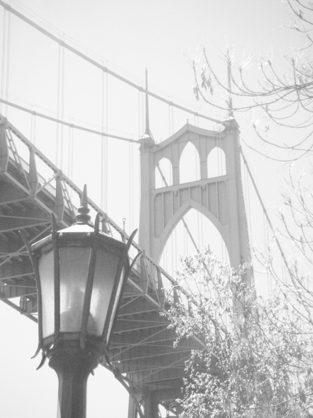 Ein altes Bild einer Hängebrücke mit einem schwarzen Laternenpfahl vorne unten und einem Baum in der rechten Ecke.
