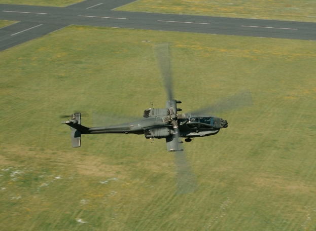Militärhubschrauber fliegt über eine grüne Wiese mit einer Straße im Hintergrund.