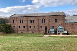 Ein großes Backsteingebäude mit einem grünen Rasen, Bäumen und einem klaren blauen Himmel, mit Fenstern, einer Tür und einer Treppe, die hinaufführt, und einer Restaurierungsmaschine auf der rechten Seite.