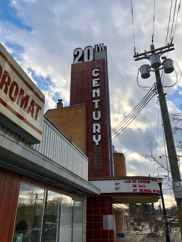 Das 20. Jahrhundert Theater in Detroit, Michigan, mit Glasw├Ąnden und Namensschildern, umgeben von B├Ąumen und Strommasten mit Dr├Ąhten unter einem bew├Âlktem Himmel.