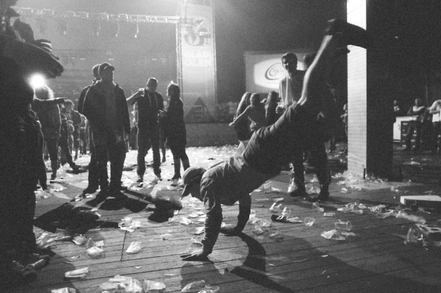 Eine Person führt eine Stunt-Show in der Mitte durch, während Zuschauer im Hintergrund stehen und Plastikteile auf dem Boden verstreut sind und ein Schild mit Text und Lichtern oben zu sehen ist.