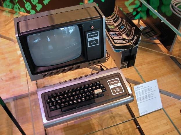 Ein Computersystem auf einem Glastisch mit einer Tafel davor, Broschüren auf der CPU und einem Holzboden im Hintergrund.