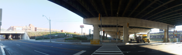Ein Lastwagen, der unter einer Brücke auf einer Stadtstraße mit umgebenen Infrastruktur und Fahrzeugen unter einem klaren blauen Himmel fährt.