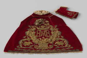 Ein roter Samtmantel mit goldener Stickerei und einer Krone, der mit aufwändigen Designs verziert ist, vor einem weißen Hintergrund.