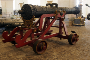 Ein altes Kanonenstück in einem Museum ausgestellt, umgeben von anderen Kanonen und Säulen im Hintergrund.
