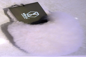 Ein weißer Pelzbeutel mit einem schwarzen Anhänger, aus Schafsfell, auf einer weißen Oberfläche.