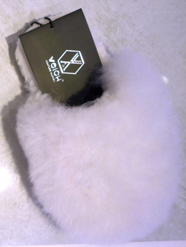 Ein weißer Pelzbeutel mit einem schwarzen Anhänger, aus Schafsfell, auf einer weißen Oberfläche.
