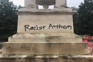 Ein Denkmal mit der Inschrift "Rassistischer Anthem" vor einem Hintergrund aus Bäumen und einem klaren Himmel.