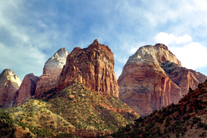 Zion National Park in Utah mit majestätischen Bergen, üppigen Bäumen, felsigem Gelände und weißen, flauschigen Wolken am Himmel.