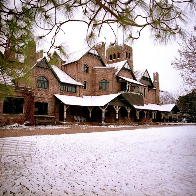 Ein Gebäude mit Fenstern, Säulen und Stühlen, mit einer Bank und einem Zweig auf der rechten Seite.