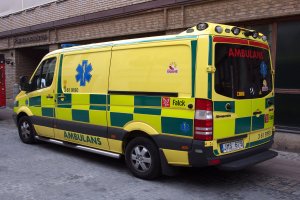 Ein Rettungswagen steht auf der Straße vor einem Backsteingebäude mit Text darauf, und ein Feuerlöscher ist auf der linken Seite des Bildes zu sehen.